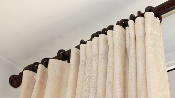 Dark wood curtain pole with curtain brackets with cream subtly patterned curtains